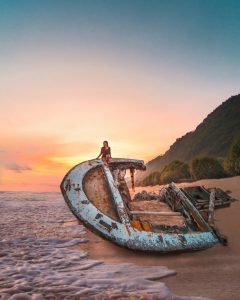 Woman sitting on the ruins of a shipwreck on a sandy beach in Bali during a colorful sunset