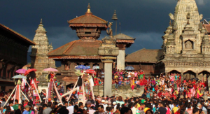 A large crowd of people celebrating Gai Jatra festival at Bhaktapur Durbar Square with historic temples in the background.