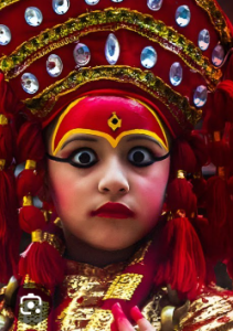 A young girl adorned as a Living Goddess (Kumari) with traditional red attire, intricate jewelry, and dramatic eye makeup.