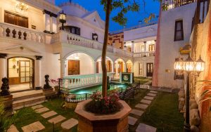 Serene twilight view of the courtyard at Baber Mahal Vilas heritage hotel in Kathmandu, Nepal, featuring a neoclassical reflecting pool, stone pathways, and arched balconies.