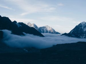Sharp, snow-capped Himalayan peaks rising above a thick layer of white clouds under a clear blue sky.