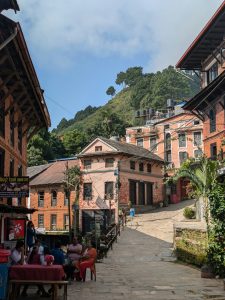 Traditional stone-paved street in Bandipur, Nepal, featuring well-preserved Newari brick buildings and a view of the surrounding green hills.