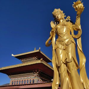 Golden Buddha statue in Paro, Bhutan, with traditional Bhutanese temple architecture under a clear blue sky.
