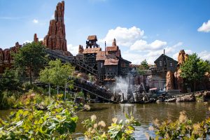 A mine train roller coaster splashing through a river in front of a red rock mountain at Big Thunder Mountain in Disneyland Paris.