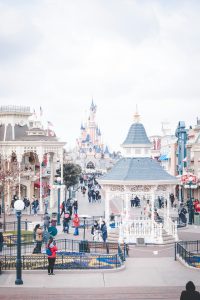 A wide view of Main Street, U.S.A. at Disneyland Paris, featuring a white Victorian gazebo in the foreground and Sleeping Beauty Castle in the distance under a bright sky.
