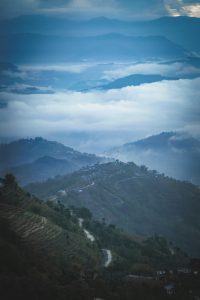 Misty mountain landscape at sunrise in Nagarkot, Nepal, with terraced fields and a winding road.