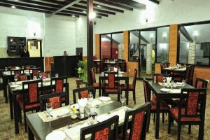 Interior of the traditional dining room at Hotel Kaze Darbar in Kathmandu, Nepal, featuring dark wood tables with red patterned chairs and exposed ceiling beams.