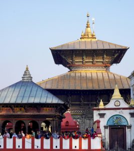 A view of the Pashupatinath Temple complex in Kathmandu, Nepal, showing the main pagoda-style temple with a gold-plated roof and other smaller structures along the Bagmati River.