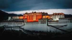 The illuminated Potala Palace at dusk, featuring grand tiered architecture under a dark, moody sky in Lhasa, Tibet.