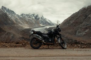 A black Royal Enfield Himalayan motorcycle parked on a dirt road with snow-capped mountains and a glacier in the background.