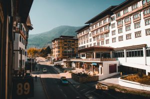 Street view of Thimphu, Bhutan, featuring traditional Bhutanese architecture, modern hotels, and scenic Himalayan mountains in the background.