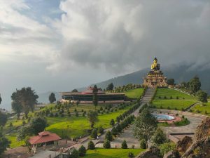 A panoramic view of the 130-foot-high golden Buddha statue at Buddha Park of Ravangla (Tathagata Tsal) in South Sikkim, India, with lush green landscapes and the Himalayas in the background. 