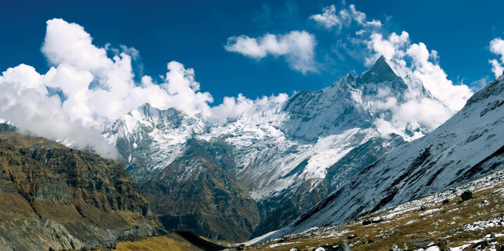  Majestic snow-capped Annapurna mountain range under a vibrant blue sky with white clouds.