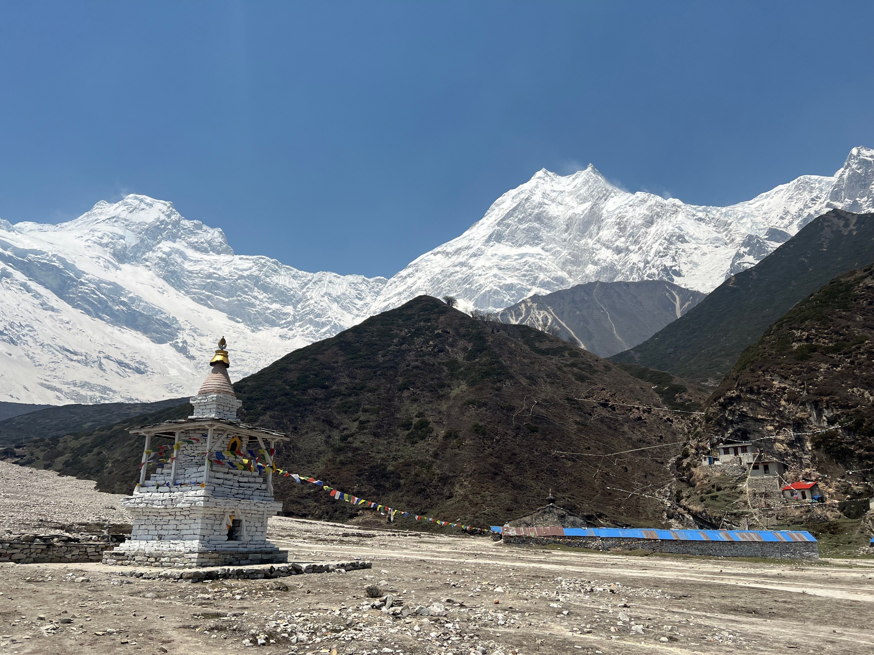 Traditional Buddhist chorten with prayer flags in front of snow-capped Mount Manaslu, Nepal.