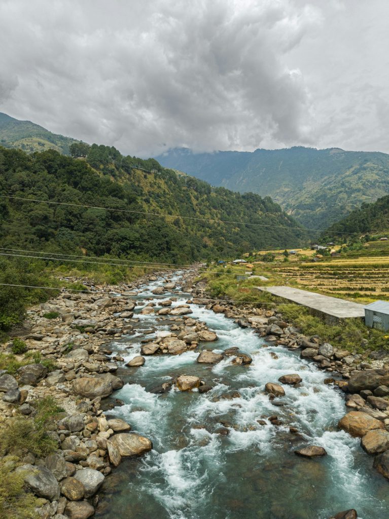 Fast-flowing rocky river in a green mountain valley under a cloudy sky.