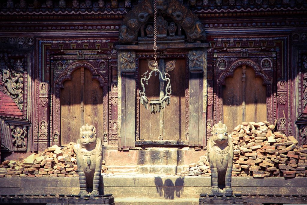Intricate Newari-style wood carvings and two stone lion statues guarding an ornate wooden doorway at the Gorkha Durbar (Gorkha Palace) complex in Gorkha, Nepal.