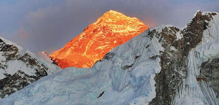 Golden morning sunlight illuminating the snow-capped peak of Mount Everest behind icy mountain ridges.