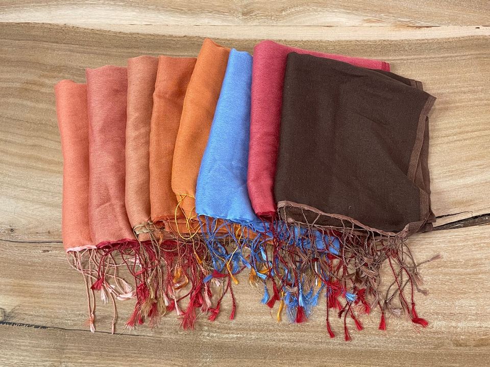 Assorted vibrant handwoven pashmina shawls from Nepal displayed on a wooden surface.