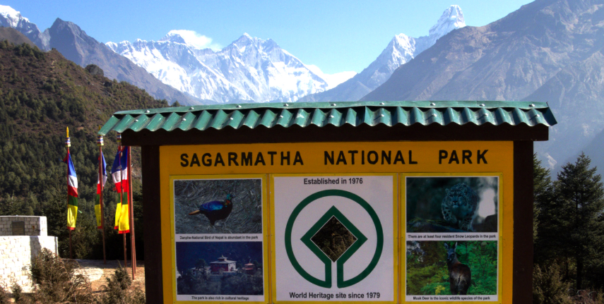 Sagarmatha National Park entrance sign with snow-capped Himalayan peaks and Mount Everest in the background.