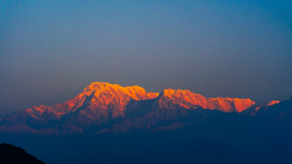 Golden sunrise light hitting the snow-capped peaks of the Annapurna range and Annapurna South as seen from the Sarangkot viewpoint in Pokhara, Nepal.