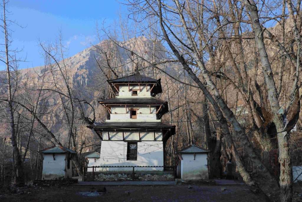  Front view of the three-tiered pagoda style Muktinath Temple in Mustang, Nepal, surrounded by bare winter trees and mountain cliffs.