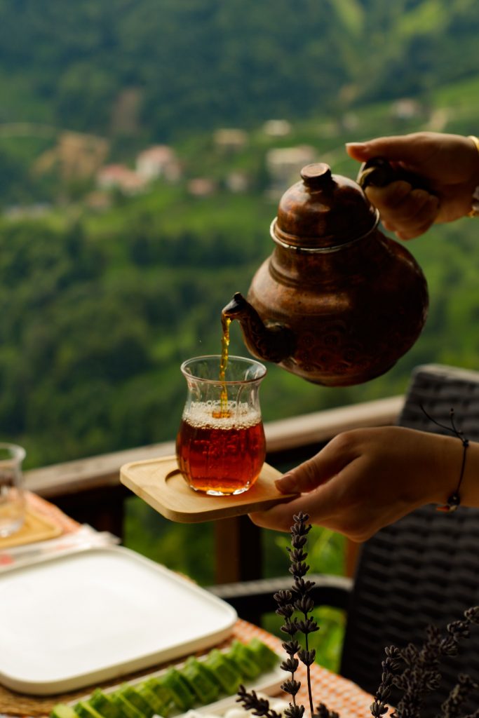 Traditional copper kettle pouring freshly brewed Nepali orthodox tea with a scenic view of Himalayan tea gardens in the background.