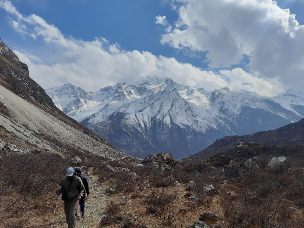 Trekkers walking a mountain path with snow-capped Langtang Lirung peaks in the background of Langtang National Park.
