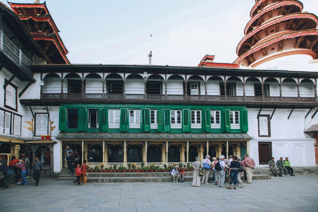 Tourists walking through Nasal Chowk courtyard at Hanuman Dhoka Durbar Square with green wooden windows and the round Panchamukhi Hanuman tower in Kathmandu.