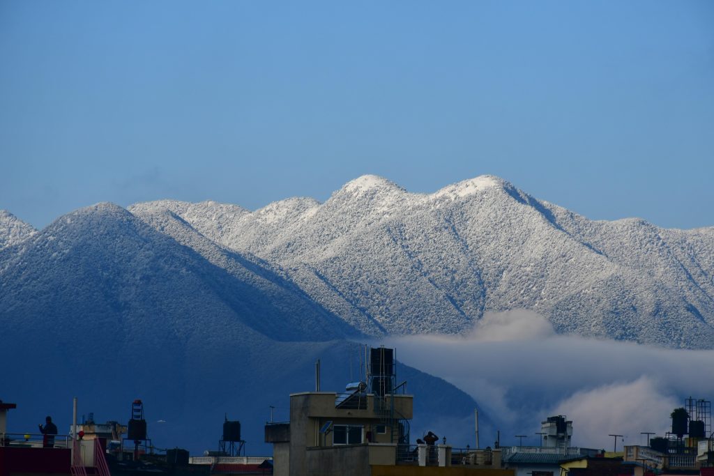 Snow-covered Chandragiri Hills and Kathmandu Valley skyline under a clear blue sky.