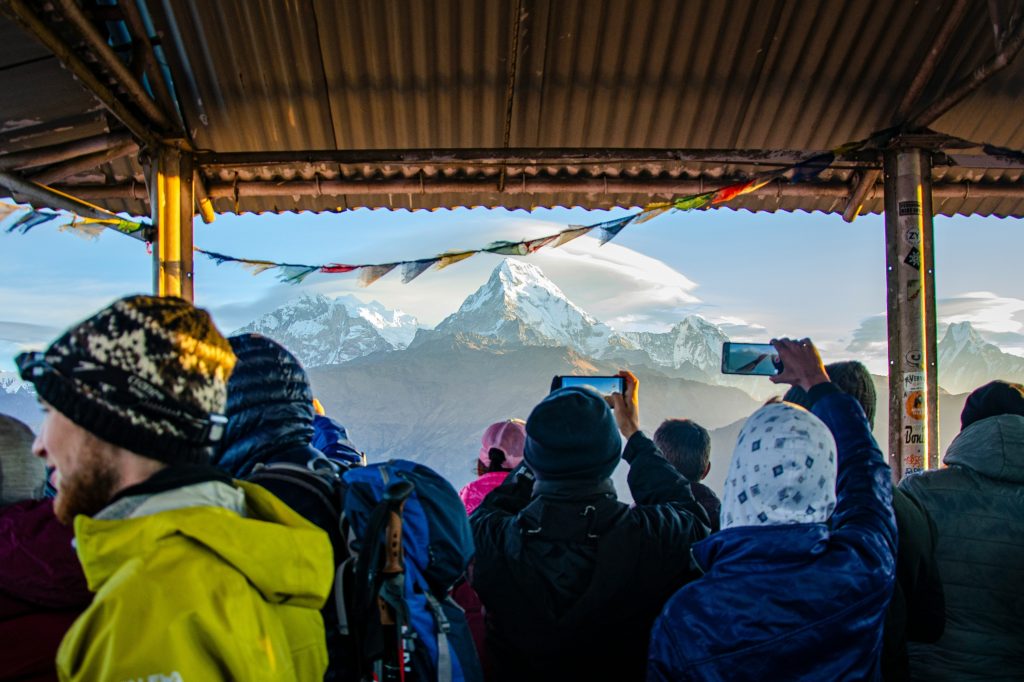 Crowd of trekkers taking photos of the sunrise over Annapurna South and Machhapuchhre from the Poon Hill viewpoint in Nepal.