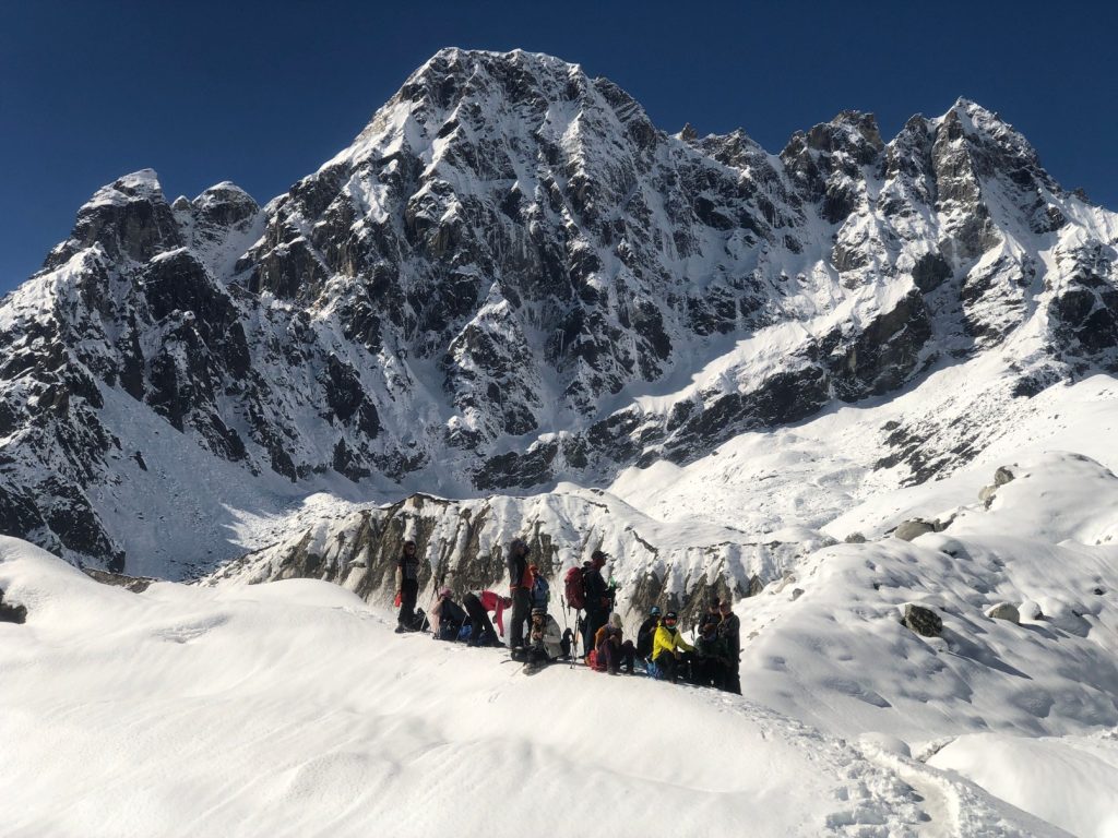 The Ultimate Guide to Adventure Activities in Nepal: Group of trekkers taking a break on the snowy Cho La Pass glacier with Cholatse peak towering in the background.