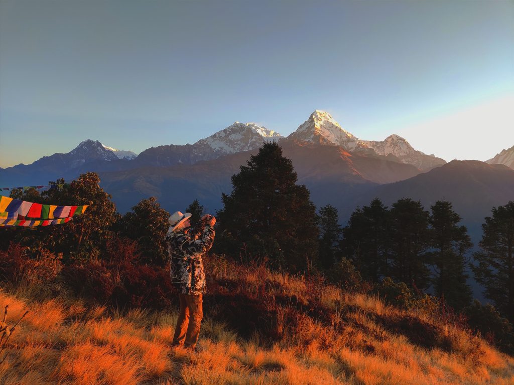 Trekker taking photos of sunrise over snow-capped Himalayan peaks at Poon Hill in Nepal