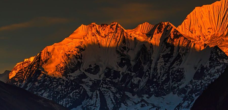 Vibrant orange sunset glowing on majestic, rugged snow-covered Himalayan mountain peaks.
